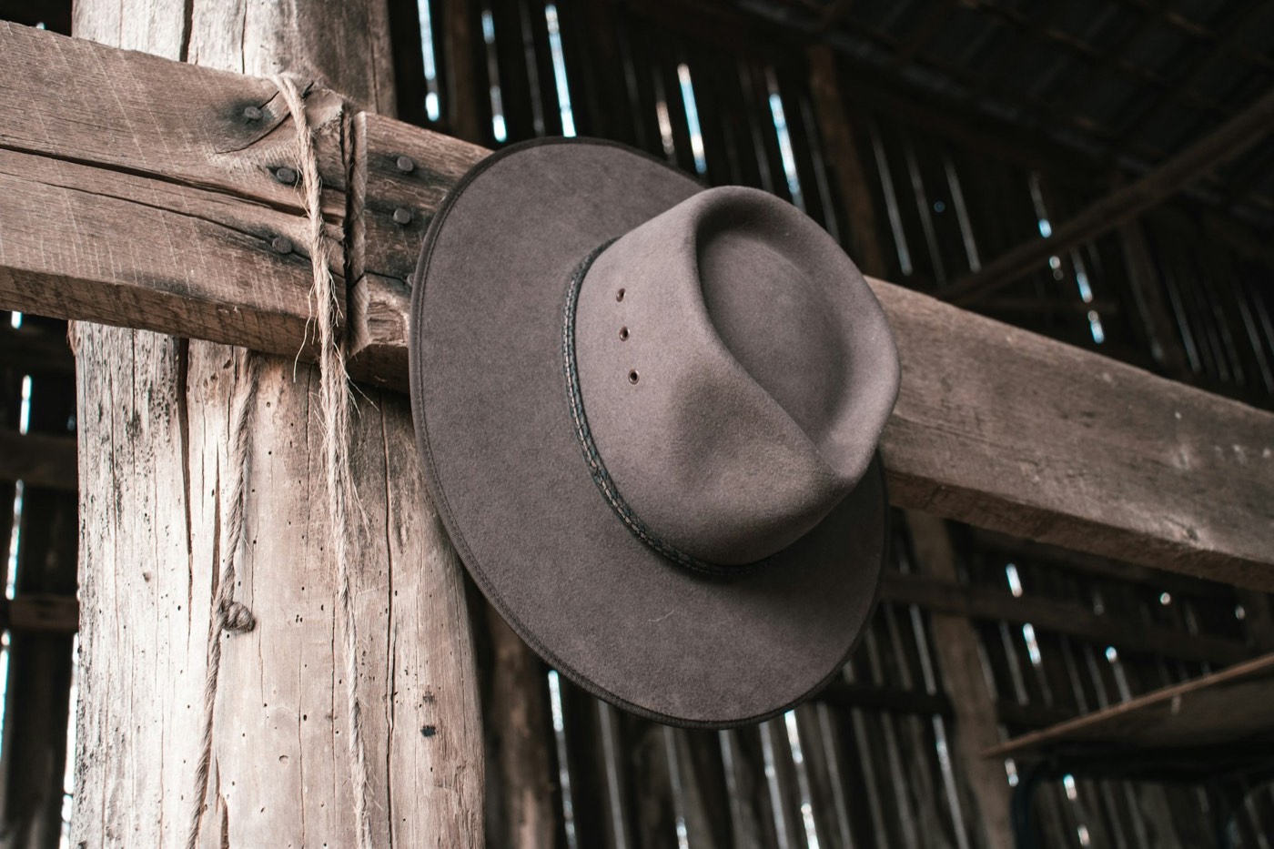 A worn felt cowboy hat hung on a post in an old barn.